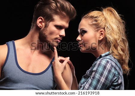 Close up of a blonde woman holding her boyfriend chin with he finger, looking at each other. On black background.