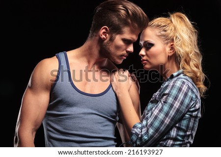 Hot blonde woman holding her hands on her boyfriend shoulder, both looking away. On studio background.