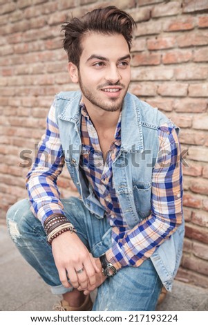 Attractive casual man posing against a brick wall, holding his hands on the wall, looking at the camera