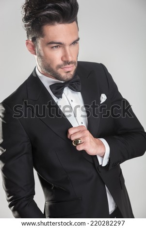 Angle view of an elegant young man ajusting his tuxedo, looking away from the camera.