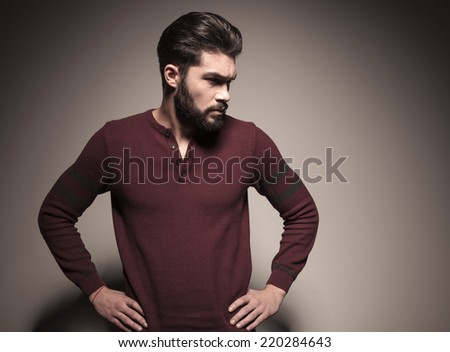 Handsome man in burgundy sweater holding his hands to his waist, looking away from the camera