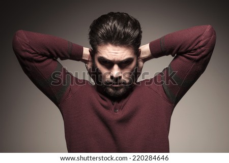 Handsome man in burgundy sweater holding both hands to his neck, looking down