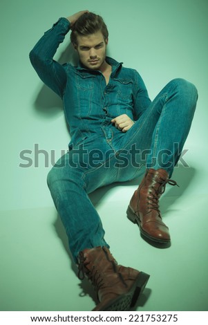 Young fashion man lying on the floor while fixing his hair, looking at the camera. Vintage look image.