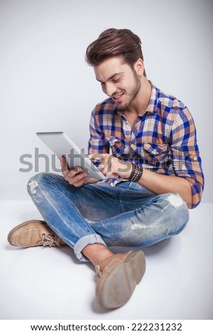 Side view of a young fashion man sitting with his legs crossed while using a tablet pad computer.