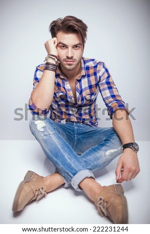 Handsome young fashion man sitting on the floor with his legs crossed while relaxing his head on his hand.