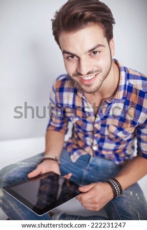 Close up picture of a young fashion man holding a tablet pad computer while smiling at the camera.