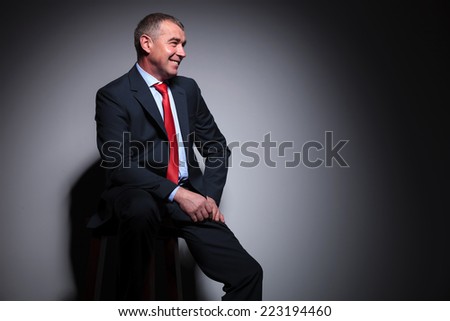 Side view of a mid aged business man sitting on a stool, lookin away from the camera.
