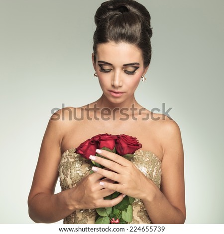 young elegant woman looking down at red roses, on grey studio background