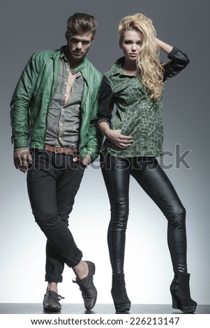 Full body image of a fashion couple posing for the camera, the woman is fixing her hair while the man is holding one hand in pocket.