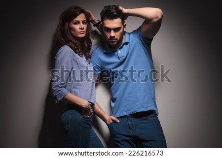 Hot fashion couple posing together, both fix their hair while looking at the camera.