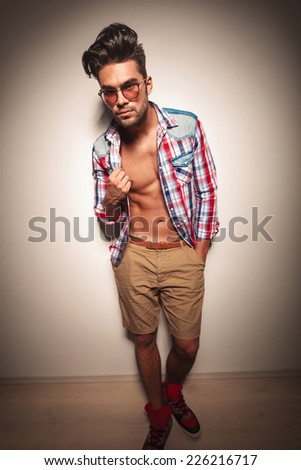 Full body image of a young fashion man pulling his shirt while looking at the camera.