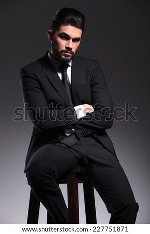 Young elegant business man holding his hands crossed while sitting on a stool, looking at the camera.
