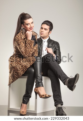 Beautiful young fashion woman sitting with her legs crossed, holding her hand to her chin while her lover is sitting and looking at her.