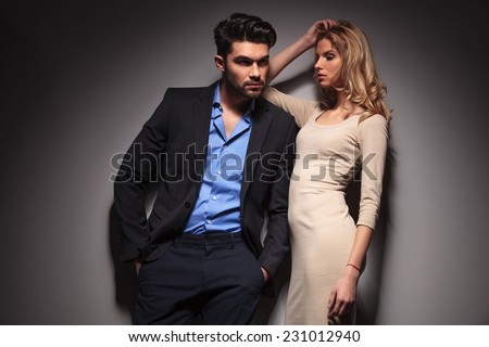 Attractive blonde fashion woman looking down while leaning her arm on her lover. The man is looking away and holding his hands in pockets.