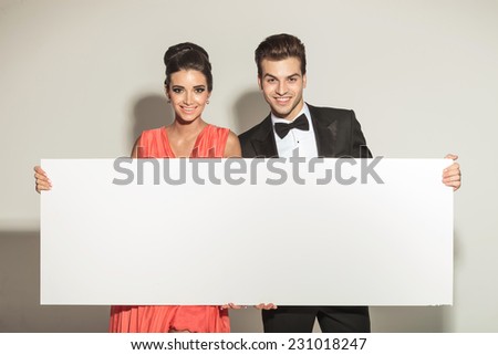 Fashion young elegant couple smiling while holding a white board.