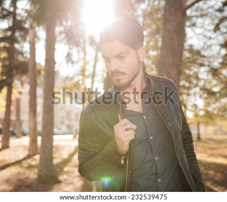 Outdoor picture of a young fashion man looking down while pulling his jacket.