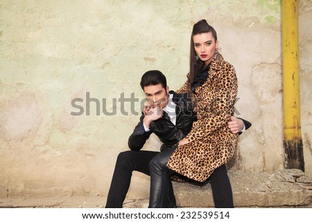 Beautiful fashion woman in a animal print coat sitting on her boyfriend lap, both looking at the camera.