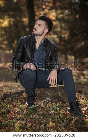 Young casual fashion man sitting on a tree stump while looking up.