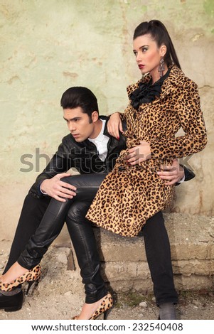 Side view of a young fashion couple sitting on old factory ruins, looking away from the camera