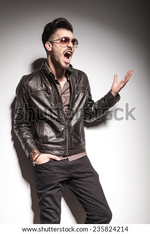 Fashion man screaming while lifting on hand in the air, against studio background.
