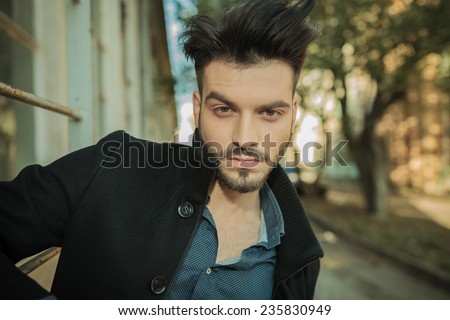 Outdoor picture of a young fashion man posing on the street, looking at the camera.
