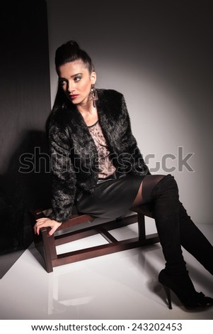 Side view of a young elegant woman looking away from the camera while sitting on a stool.