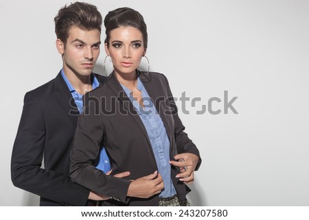 Picture of a young fashion couple posing together. The man is holding the woman from behind.