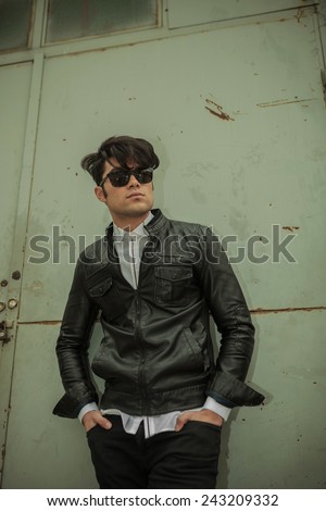 Down view of a young fashion man holding both hands in pocket while leaning on a green metal door.