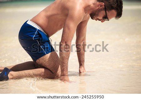 Side view picture of a young man on the beach, on his knee, looking down.
