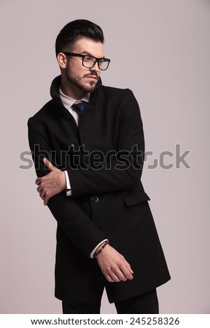 Elegant business man holding his right arm with his left hand while looking away from the camera.
