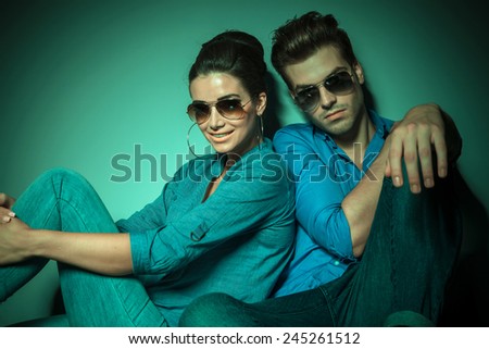 Fashion woman smiling and holding her leg with both hands while her boyfriend is leaning on her, both sitting.