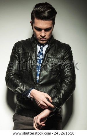 Business man in leather jacket, looking down while fixing his sleeve. On grey studio background.