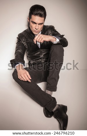 Casual fashion man sitting on the floor while looking away from the camera, holdinh both hands on his knees.
