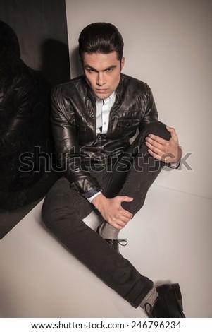 Young casual man sitting on the floor holding his leg with both hands, looking at the camera.