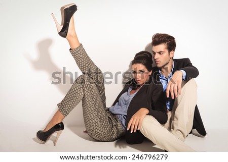 Sexy fashion woman leaning on her lover and holding one leg up while he is looking away from ther camera. Both are sitting on ther floor.