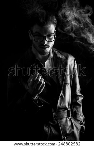 Black and white image of a attractive young fashion man holding one hand in his pocket while enjoying a cigarette.