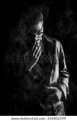 Portrait of a fashion man fixing his belt while looking down and smoking a cigarette.