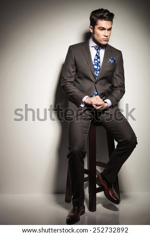 Full body picture of a young business man sitting on a stool while looking down thinking.