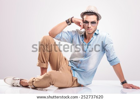 Young casual man sitting on the floor leaning his hand on his knee, looking at the camera