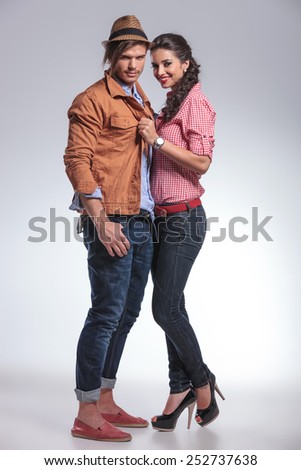 Happy fashion couple posing together on studio background. She is pulling his jacket.