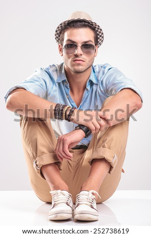 Fashion man resting on the floor with his knees up, holding his hands together while looking at the camera.