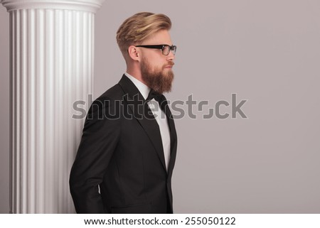 Side view picture of a elegant blonde business man posing near a white column.