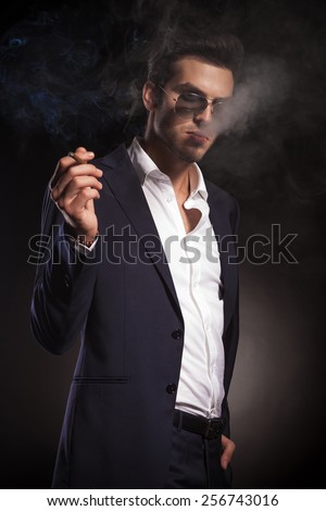 Side view of a young elegant business man holding one hand in his pocket while smoking a cigarette.