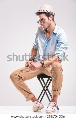 Side view of a casual fashion man sitting on a stool while looking down.