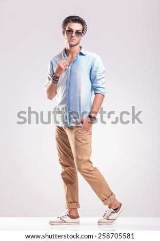 Full body picture of a casual fashion man stepping forward while fixing his collar.