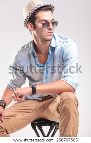 Attractive fashion man resting on a stool while looking to his side, holding his hand on his knee.