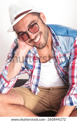 Happy young fashion man sitting on the floor while leaning his head on his hand.