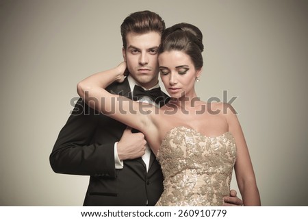 Elegant woman looking down while holding her hand around her husbands neck.