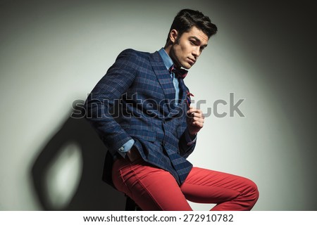 Side view of a handsome fashion man looking down while sitting on a chair with his hand in pocket.