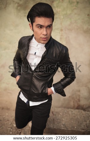 Picture of a casual fashion man posing with his hands in pockets near a old wall.